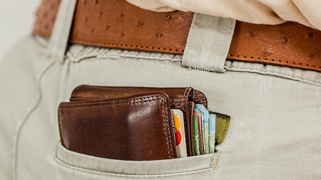 Eine Brieftasche mit Kreditkarten und Geldscheinen ragt aus einer Hosentasche hervor.