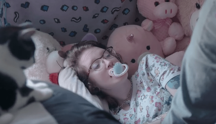 Frau mit Schnuller im Mund liegt im Bett.