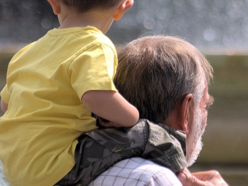 Ein Großvater trägt seinen Enkel Huckepack auf den Schultern.