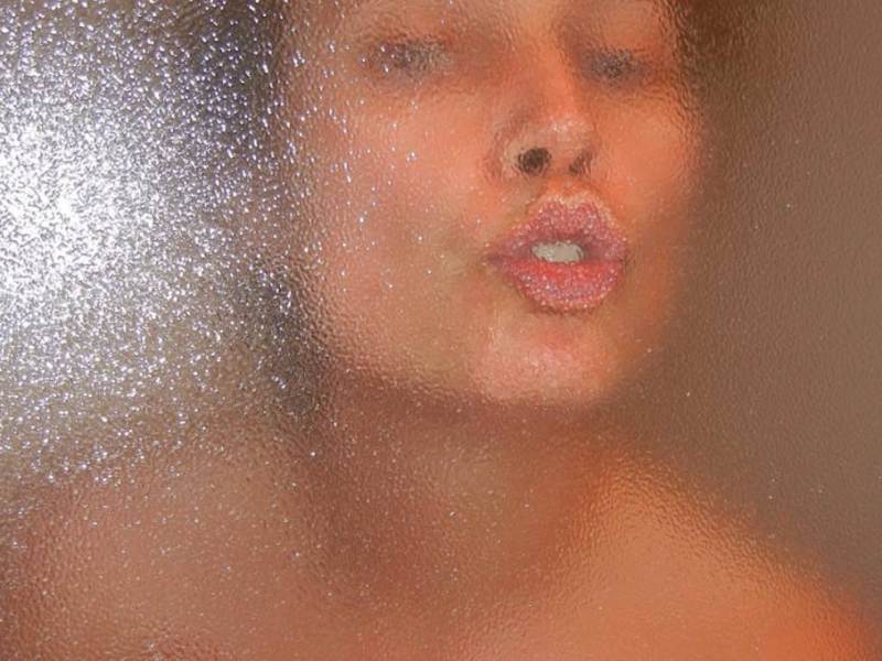Eine Frau küsst die Scheibe einer Dusche von innen.