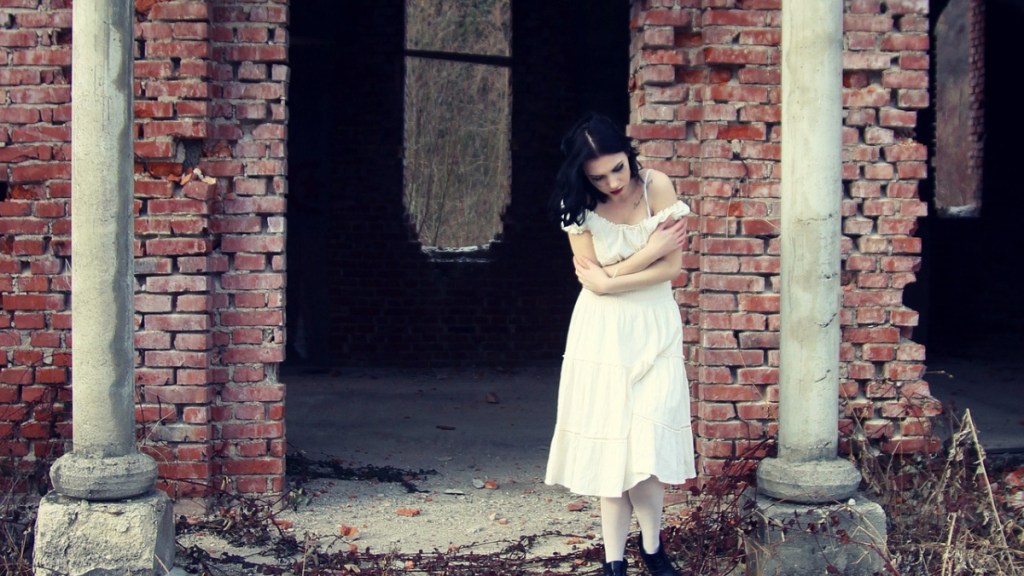 Eine Frau mit weißem Kleid steht vor einer Ruine.