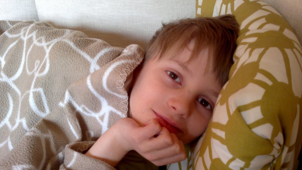 Ein blonder Junge liegt lächelnd im Bett.