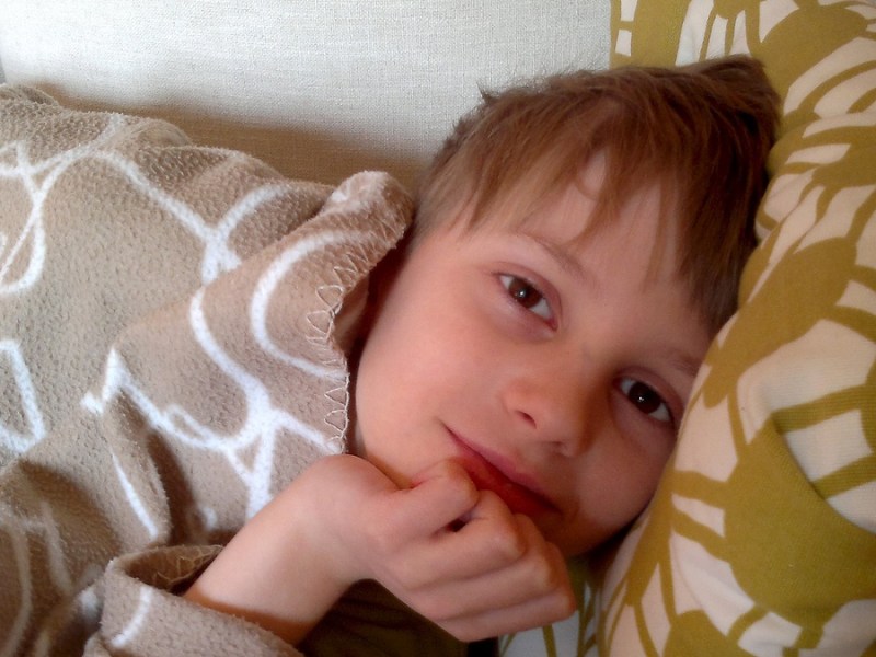 Ein blonder Junge liegt lächelnd im Bett.