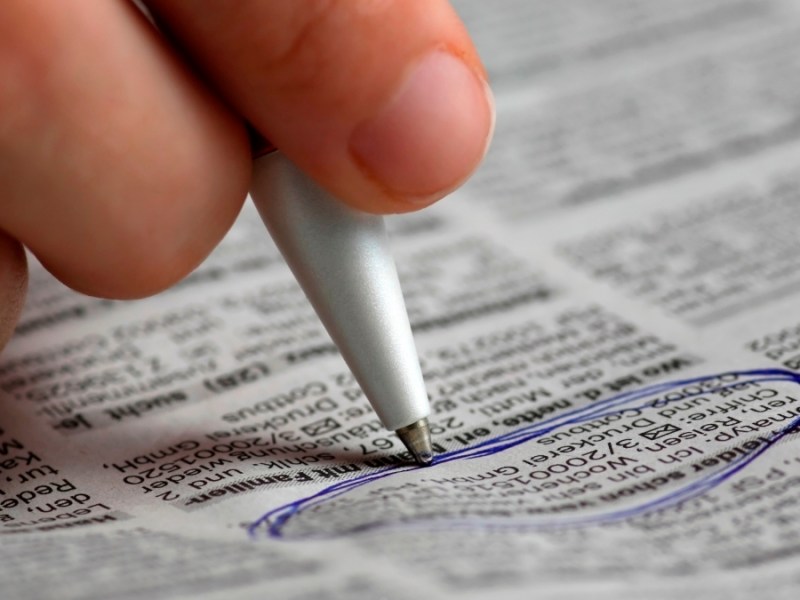 Eine Hand markiert mit einem Kugelschreiber eine Kleinanzeige in einer Zeitung.