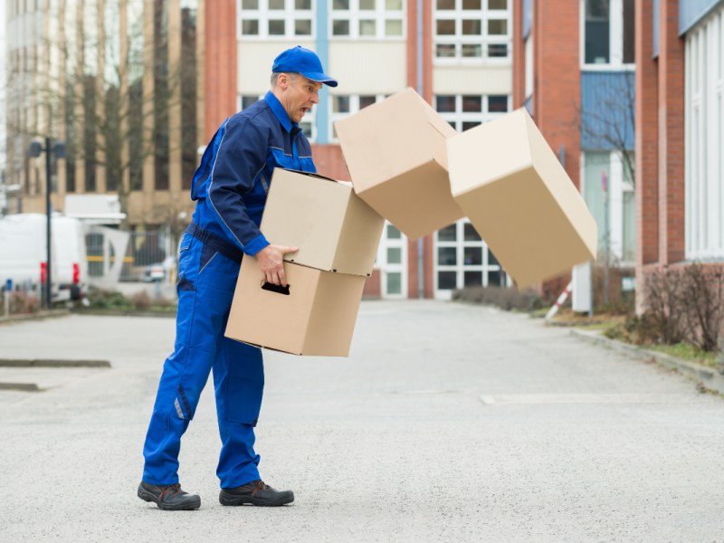 Einem Postbote fallen beim Ausliefern Pakete vom Stapel.