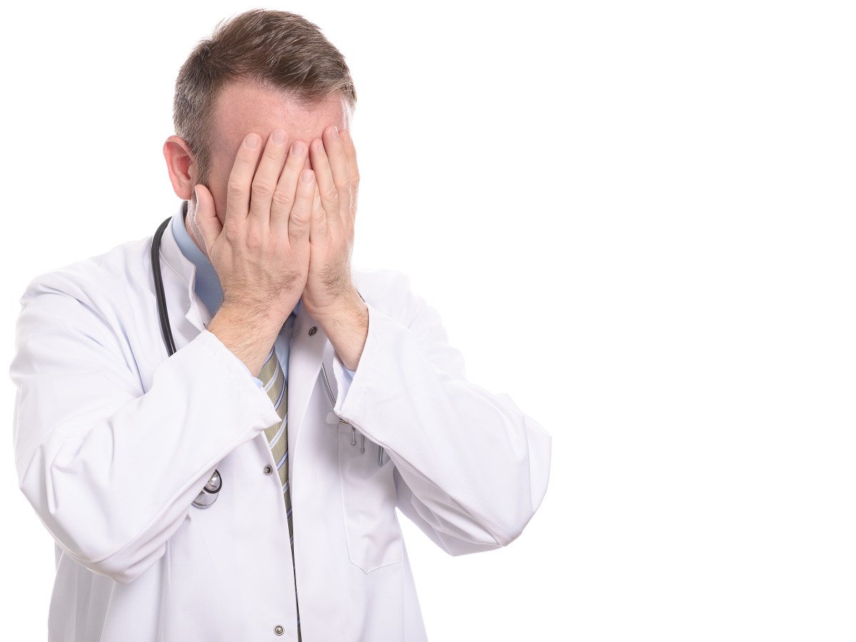 Ein Arzt mit Stethoskop und weißem Kittel schlägt verzweifelt die Hände vors Gesicht.