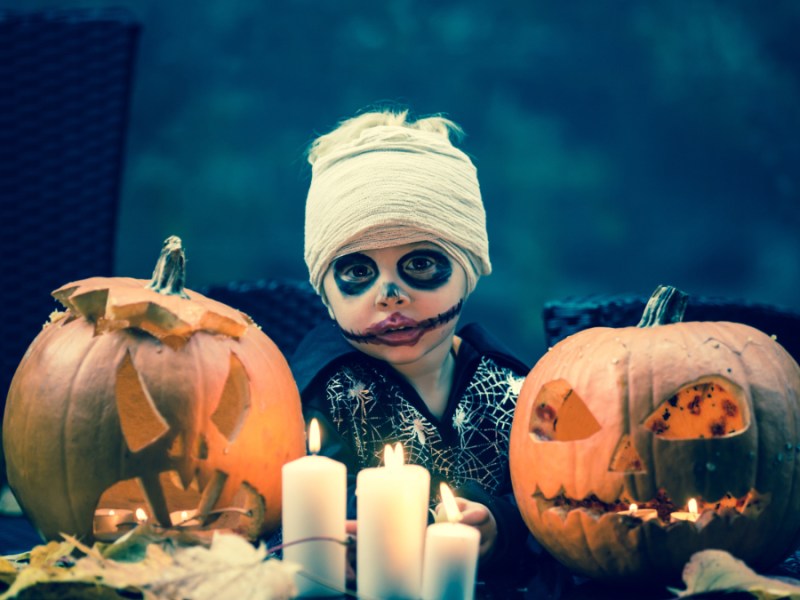 Ein Bild von einem Jungen in einem gruseligen Halloween-Kostüm, der vor Kürbis-Lampen sitzt.