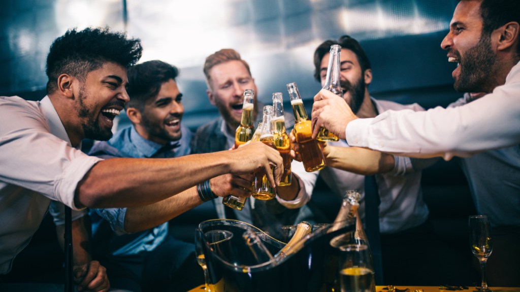 Junge Männer stoßen mit ihren Getränken auf einer Party an.
