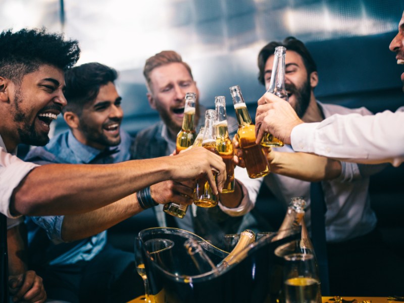 Junge Männer stoßen mit ihren Getränken auf einer Party an.