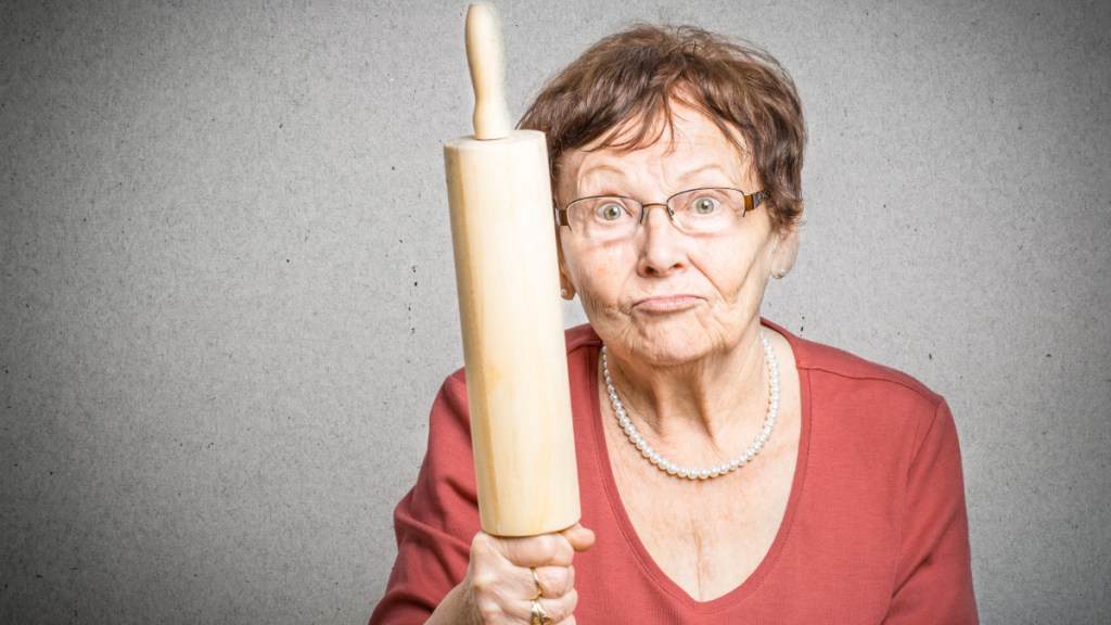 Eine wütende Frau hält drohend ein Nudelholz in der Hand.