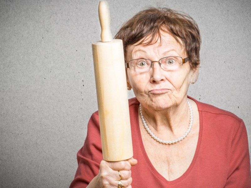 Eine wütende Frau hält drohend ein Nudelholz in der Hand.