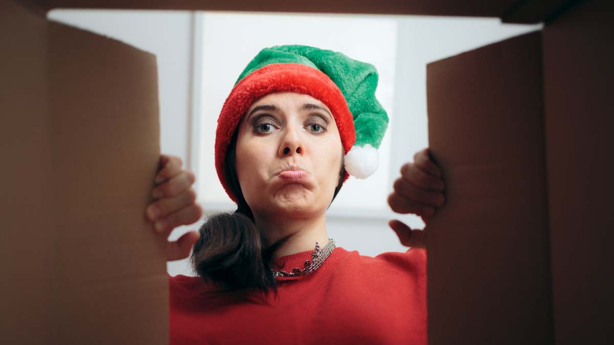 Eine Frau öffnet ein Geschenk an Weihnachten und macht ein enttäuschtes Gesicht.