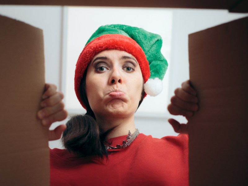 Eine Frau öffnet ein Geschenk an Weihnachten und macht ein enttäuschtes Gesicht.