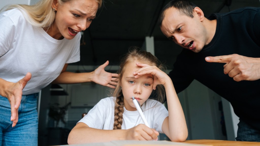 Zwei wütende Eltern schimpfen mit ihrer Tochter, die gerade ihre Hausaufgaben macht.