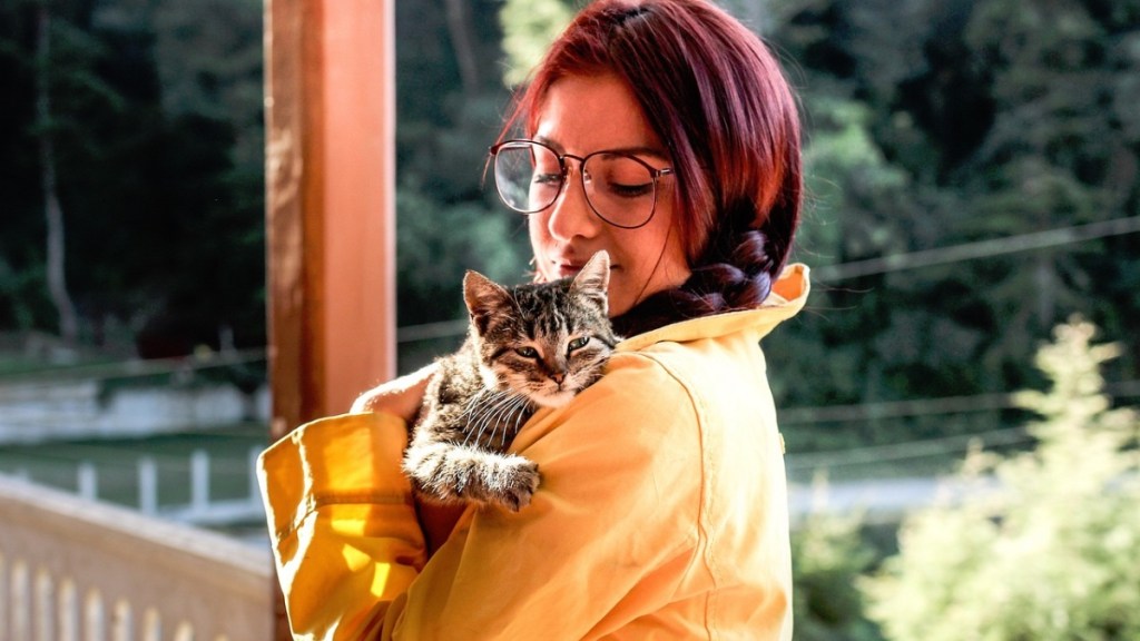Eine junge Frau mit roten Haaren hält eine Katze im Arm.