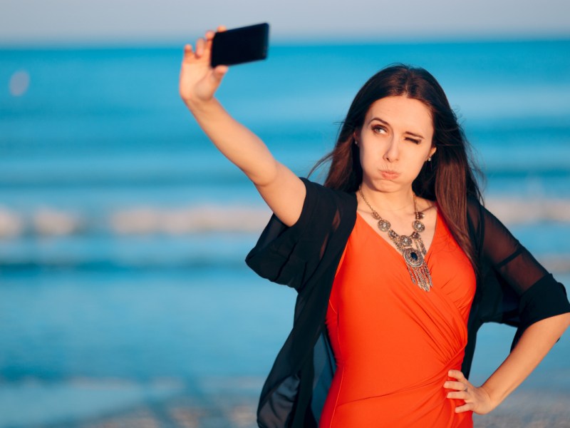 Eine junge Frau macht ein Selfie an einem Strand.