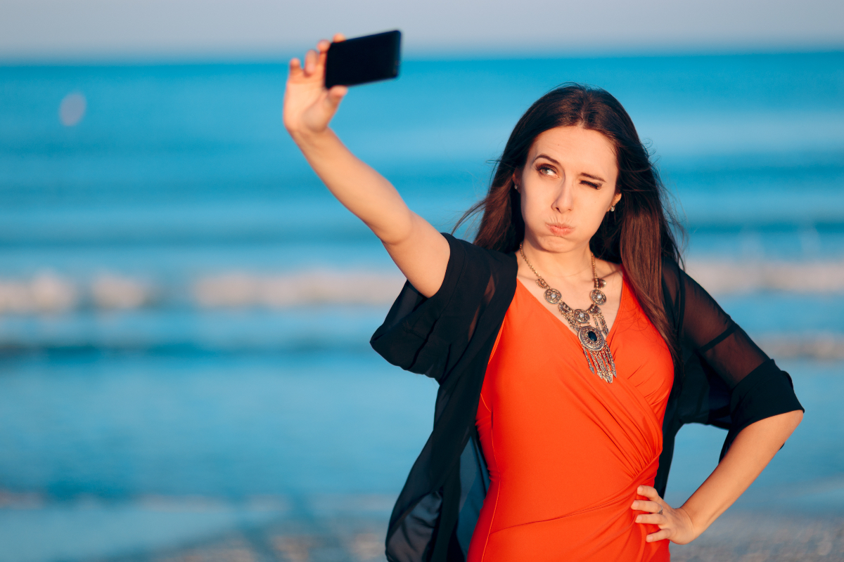 Eine junge Frau macht ein Selfie an einem Strand.