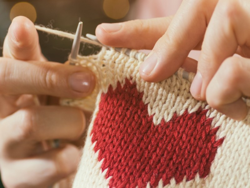Frau strickt das rote Herz für ihren Liebsten.