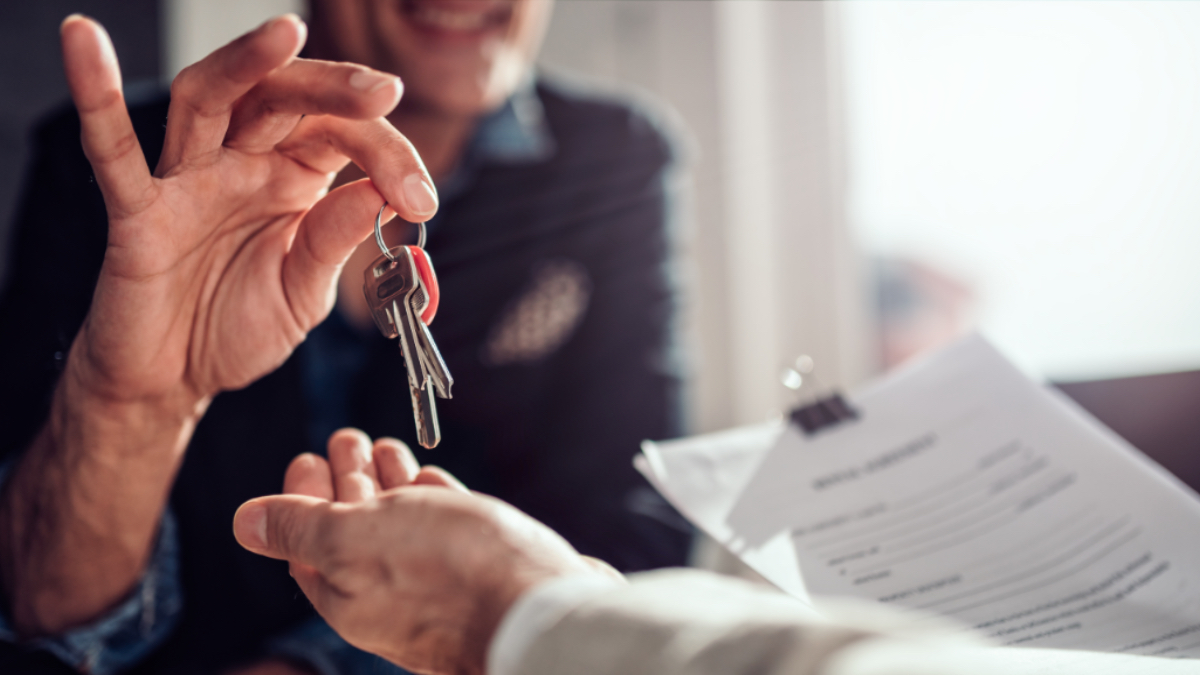Ein Vermieter übergibt einen Schlüssel an einen Mieter, der einen Mietvertrag in der Hand hält.