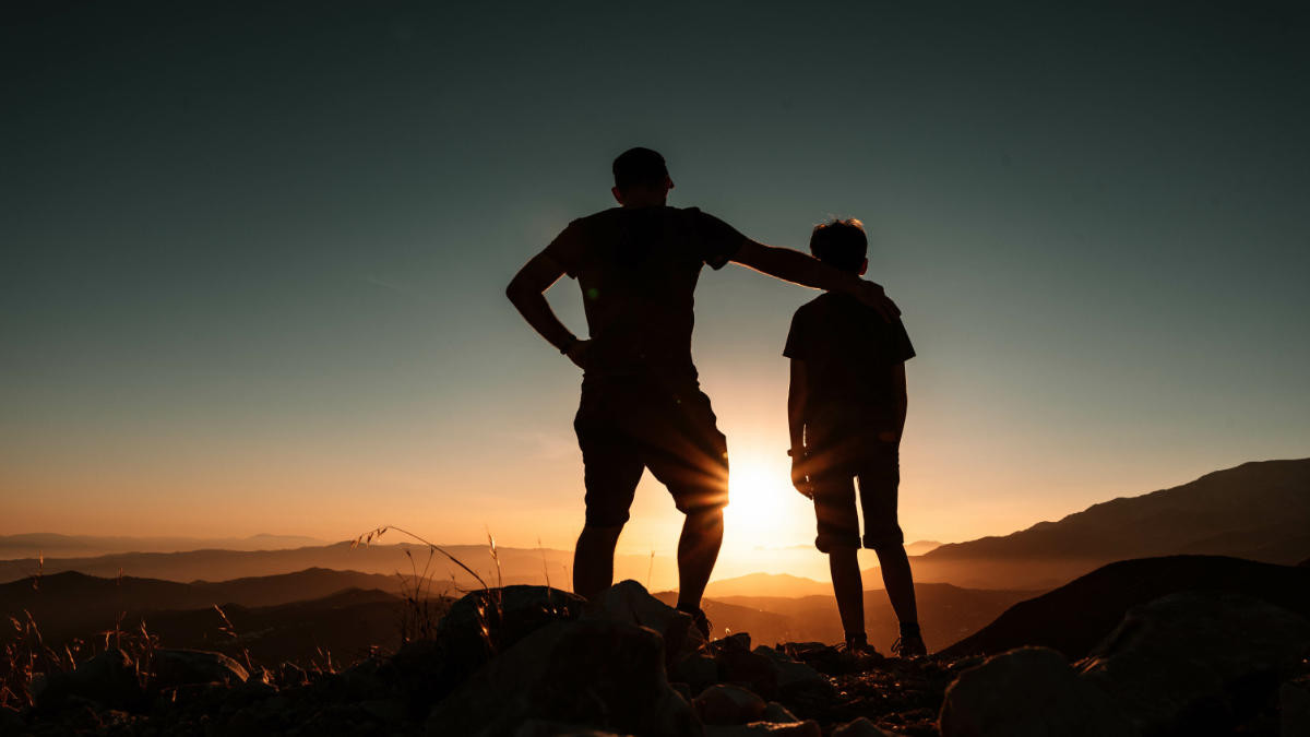 Die Silhouetten eines Vaters und eine Sohnes vor einem Sonnenuntergang.