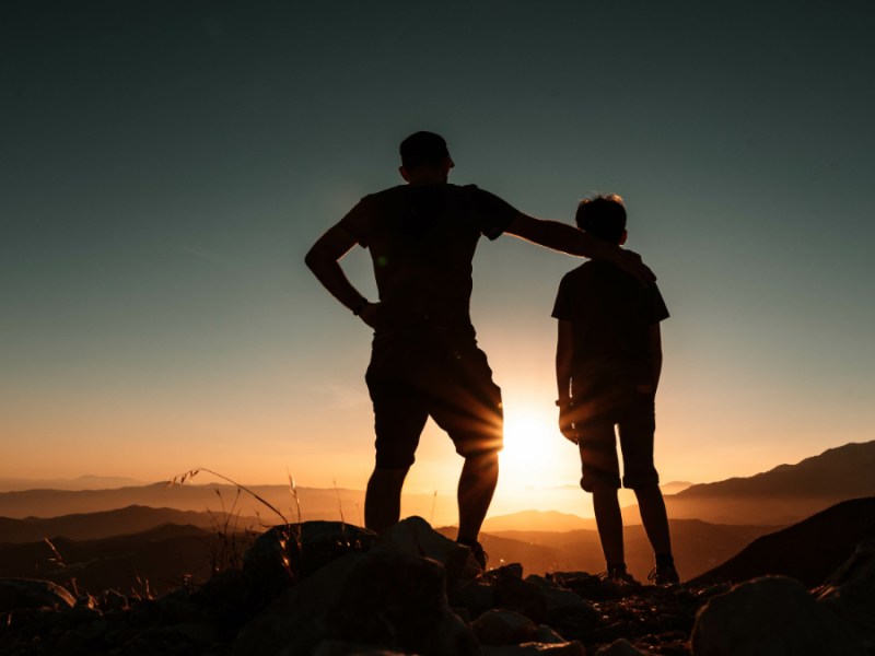 Die Silhouetten eines Vaters und eine Sohnes vor einem Sonnenuntergang.