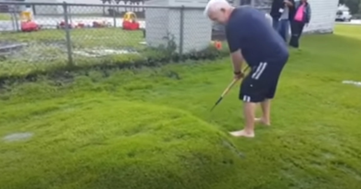Ein Mann sticht in eine Beule auf seinem Rasen.