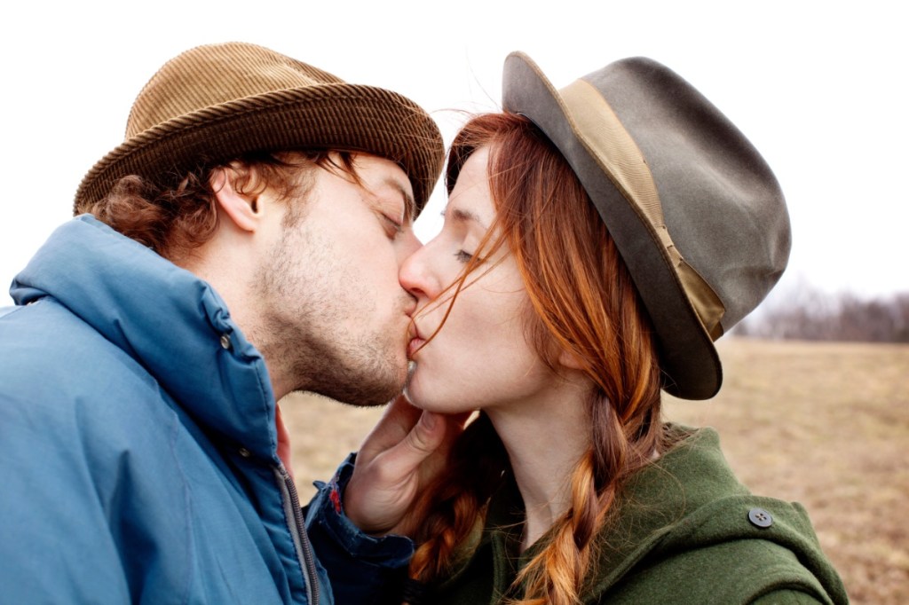 Ein junger Mann und eine junge Frau küssen sich auf einem Feld.