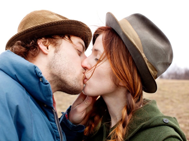 Ein junger Mann und eine junge Frau küssen sich auf einem Feld.