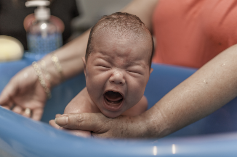 Eine Frau badet ein schreiendes Baby in einer blauen Wanne