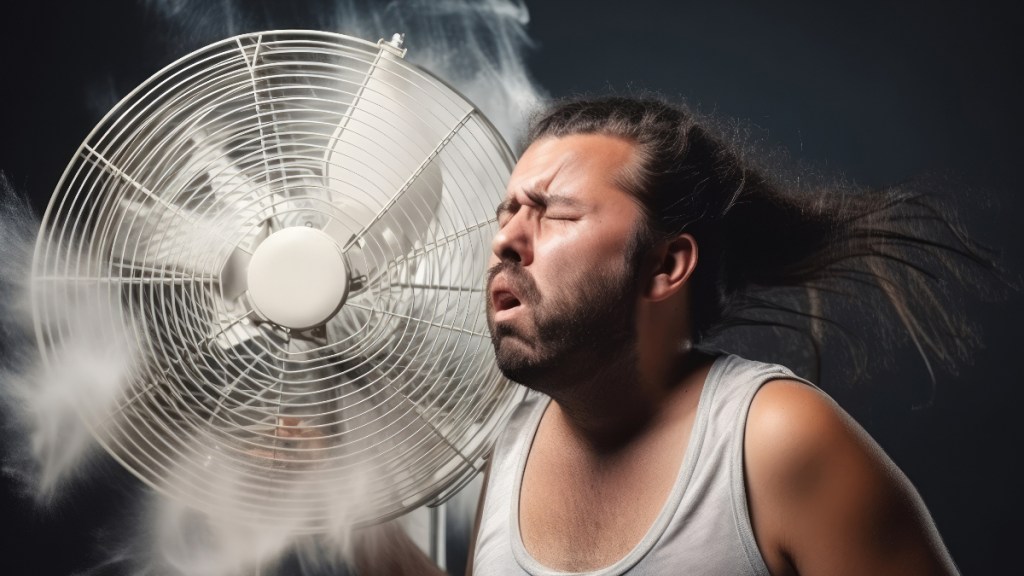 Ein Mann im Unterhemd steht vor einem Ventilator, um sich abzukühlen.