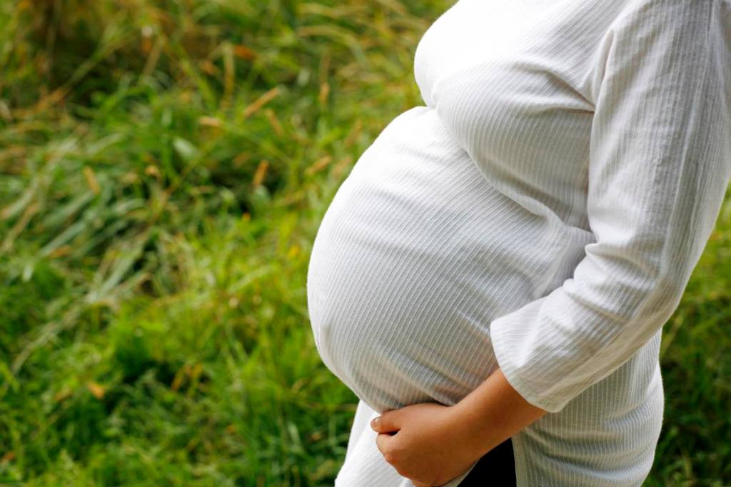 Eine schwangere Frau auf einer Wiese hält sich den Bauch.