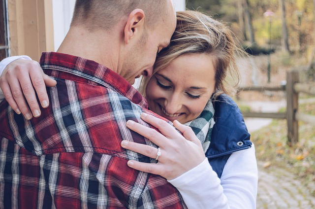 Ein Mann im Karohemd und eine blonde Frau mit Jacke laecheln und umarmen sich