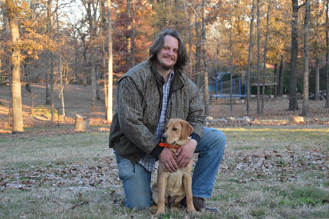 Ein Mann posiert mit einem Hundewelpen im Wald fuer ein Foto