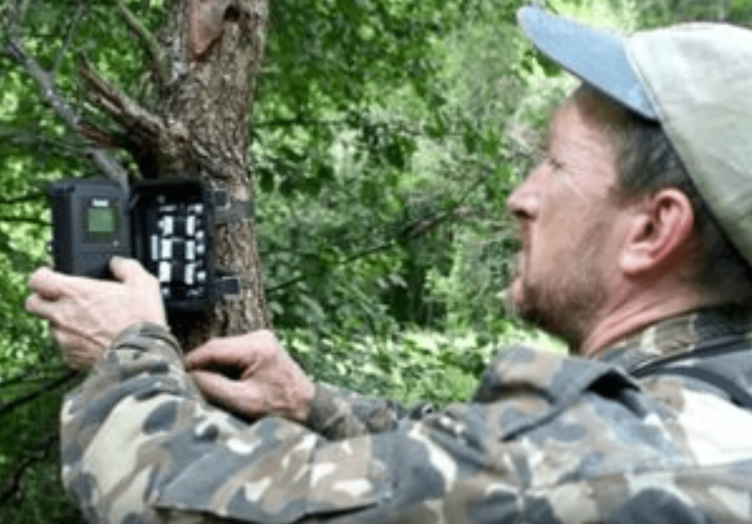 Ein Mann in Tarnkleidung stellt eine Kamera im Wald auf.