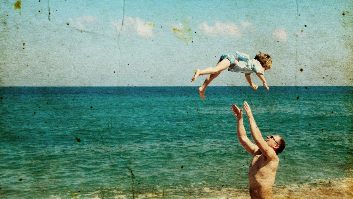 Ein altes Foto von einem Vater, der mit seinem Kind am Strand spielt.