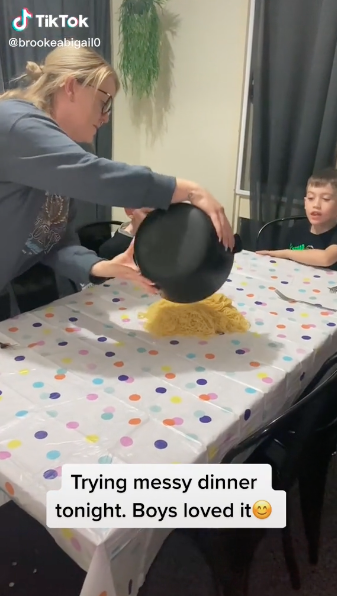 Eine Mutter kippt für ihre Kinder Spaghetti auf den Tisch.