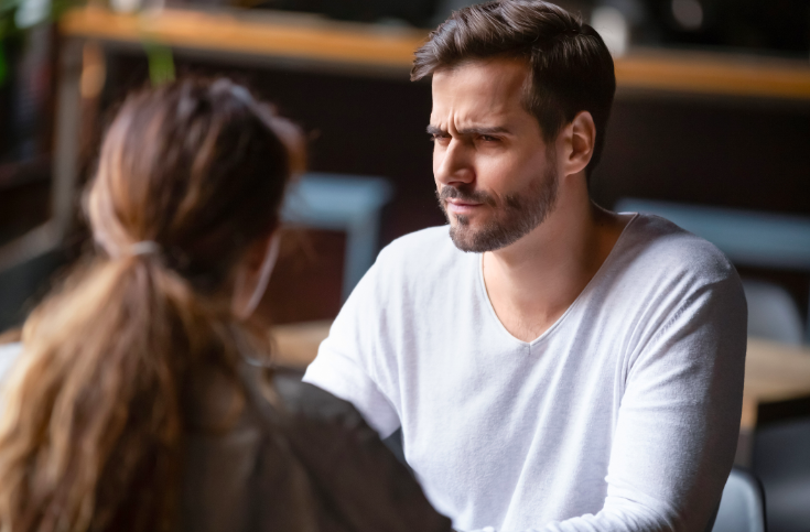 Mann schaut skeptisch zu Partnerin gegenüber am Tisch