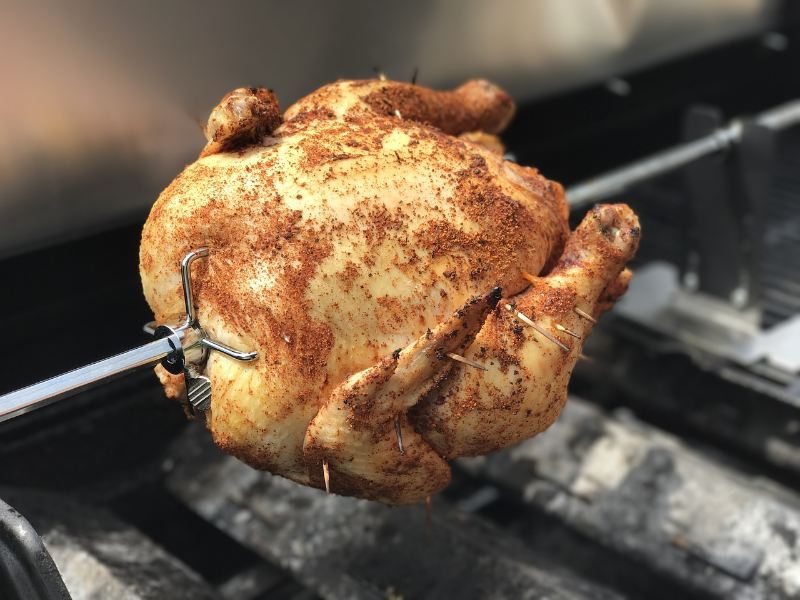 Ein Grillhähnchen steckt an einem Bratspieß am Grill