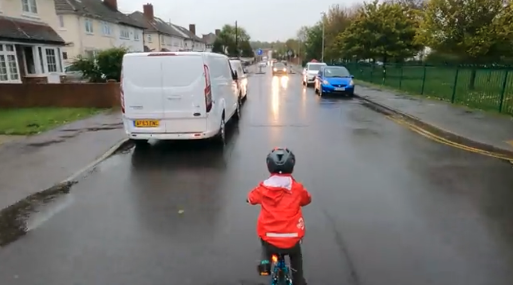 Ein Kind mit Fahrradhelm fährt auf der Mitte einer Straße