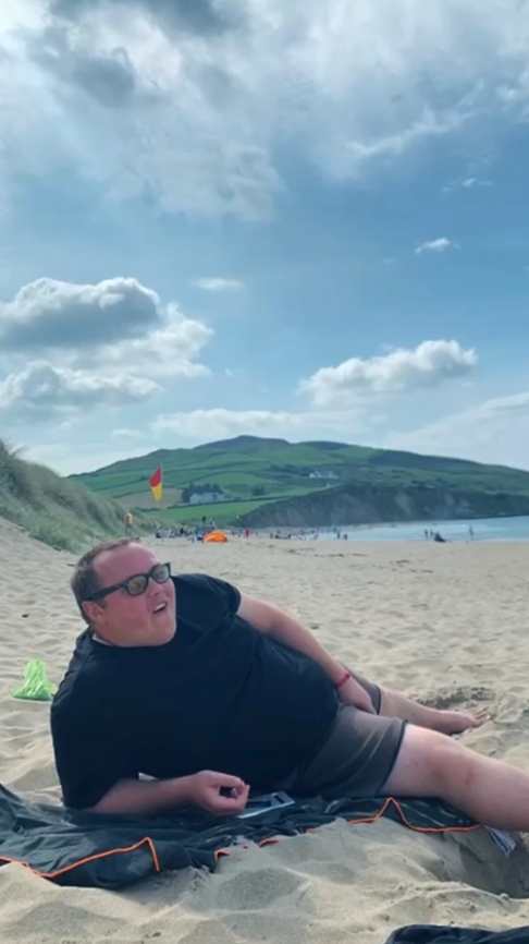 Ein Mann mit kurzer Hose und Sonnenbrille liegt am Strand.