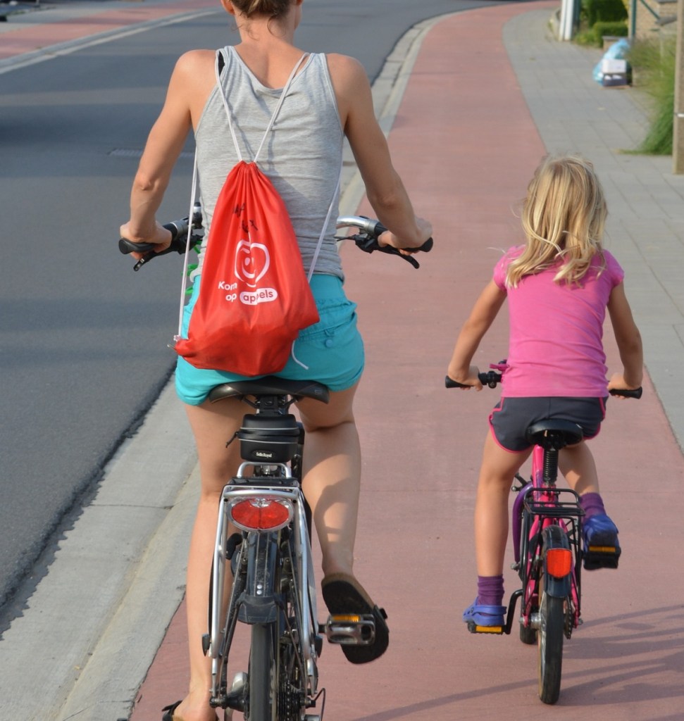 Eine Mutter fährt mit ihrer kleinen Tochter Fahrrad auf einem roten Radweg.