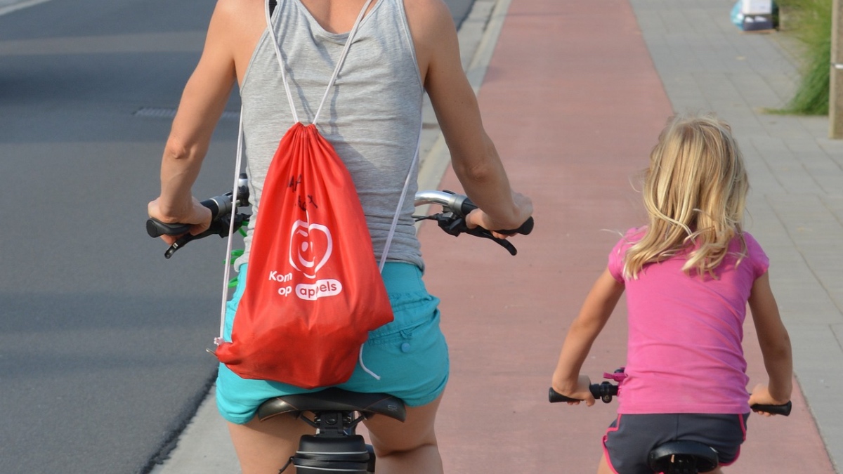 Eine Mutter fährt mit ihrer kleinen Tochter Fahrrad auf einem roten Radweg.