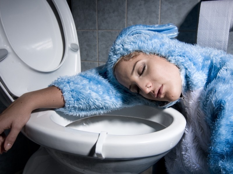 Eine betrunkene Frau in einem blauen Kostüm liegt mit dem Kopf auf einer Toilettenschüssel.