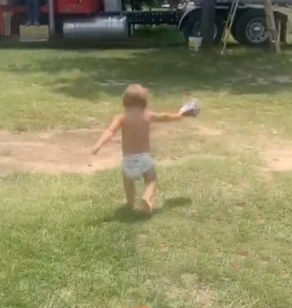 Ein Kleinkind läuft über eine Wiese und wirft dabei seine Mütze von sich