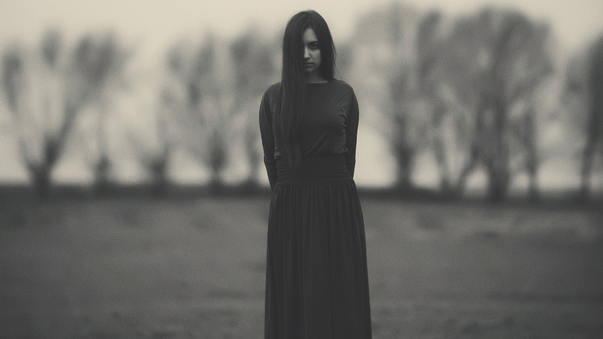 Ein Schwarzweiß-Foto von einem Mädchen in einem langen Kleid, das auf einem Feld steht.