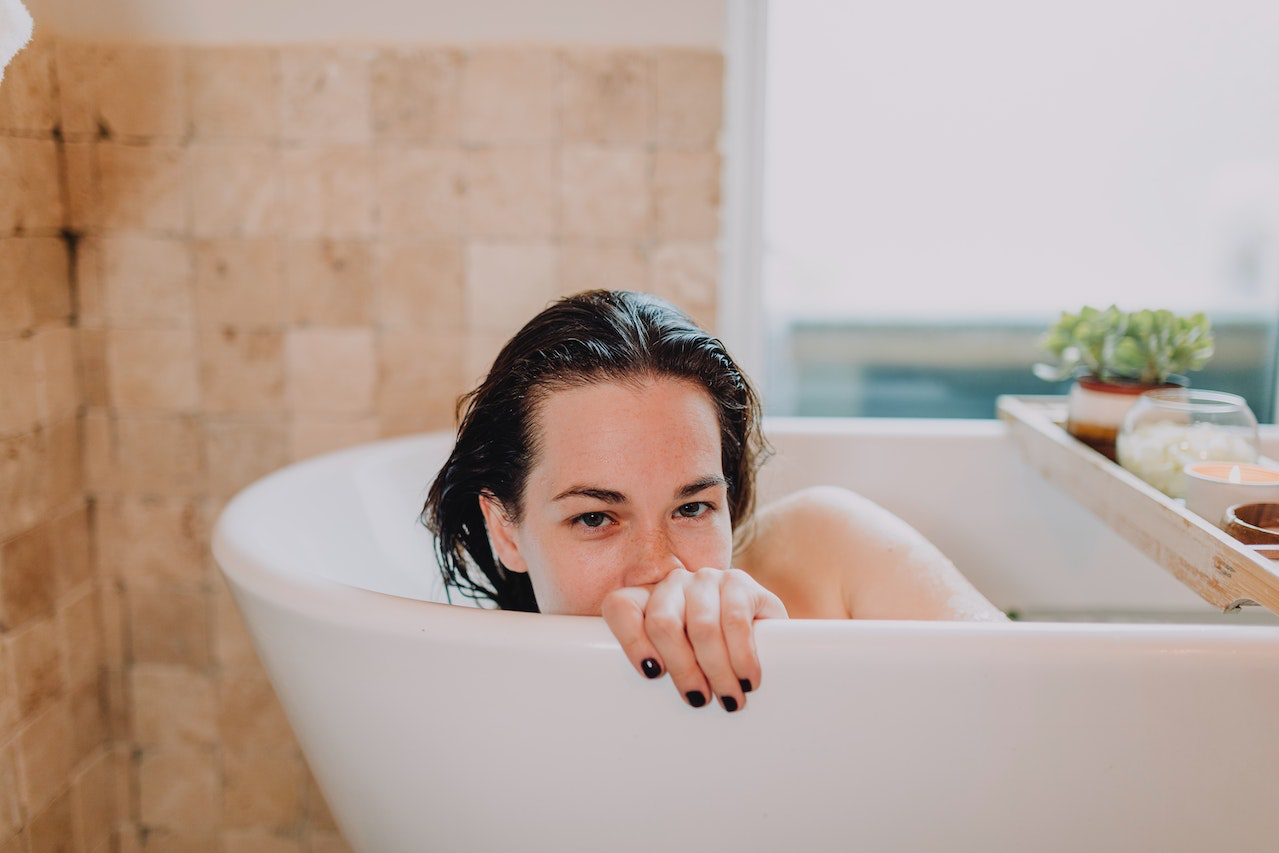 Eine Frau liegt mit nassen Haaren in einer weißen Badewanne und hält sich am Rand fest.