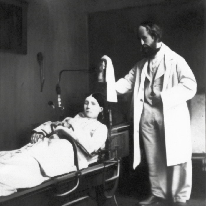 Ein Schwarz-Weiß-Bild von einer Frau im Krankenbett. Neben ihr steht ein bärtiger Arzt im weißen Kittel.