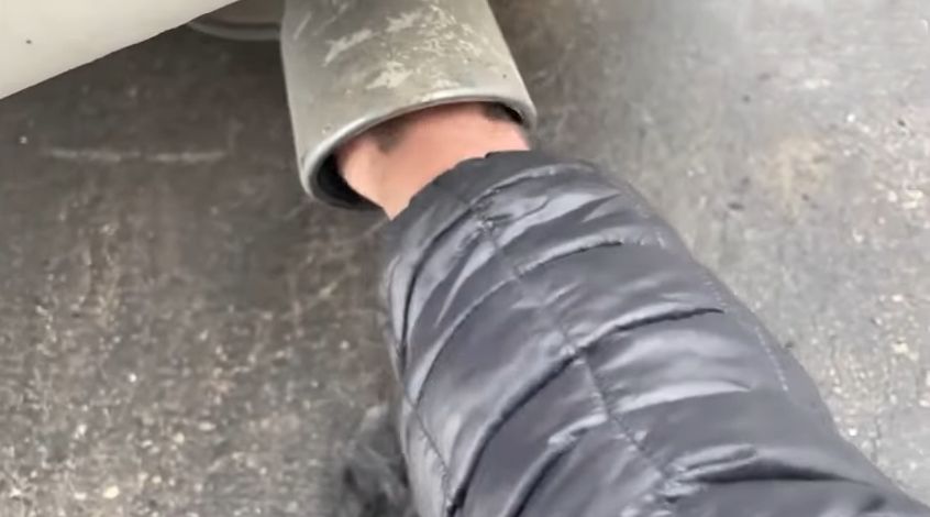 Eine Hand greift in das Auspuffrohr eines Autos hinein.