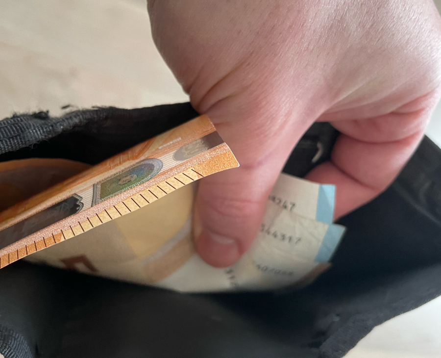 Eine Hand greift in ein Portemonnaie mit Geldscheinen.