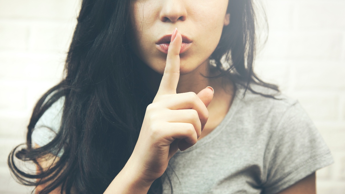 Eine junge Frau hält sich den Zeigefinger vor die Lippen.